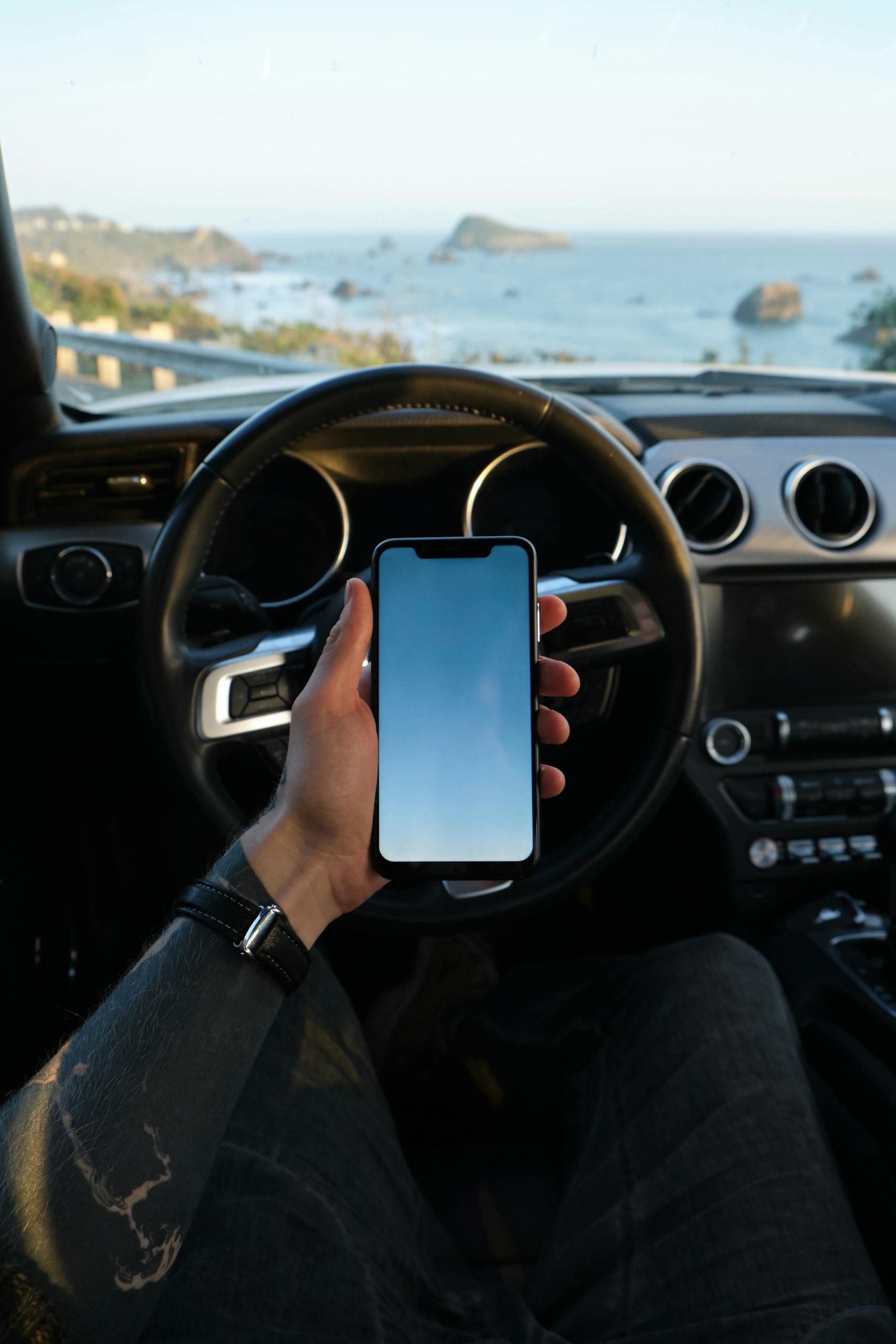 A man uses his smartphone while parked by the seaside, capturing a modern travel lifestyle.
