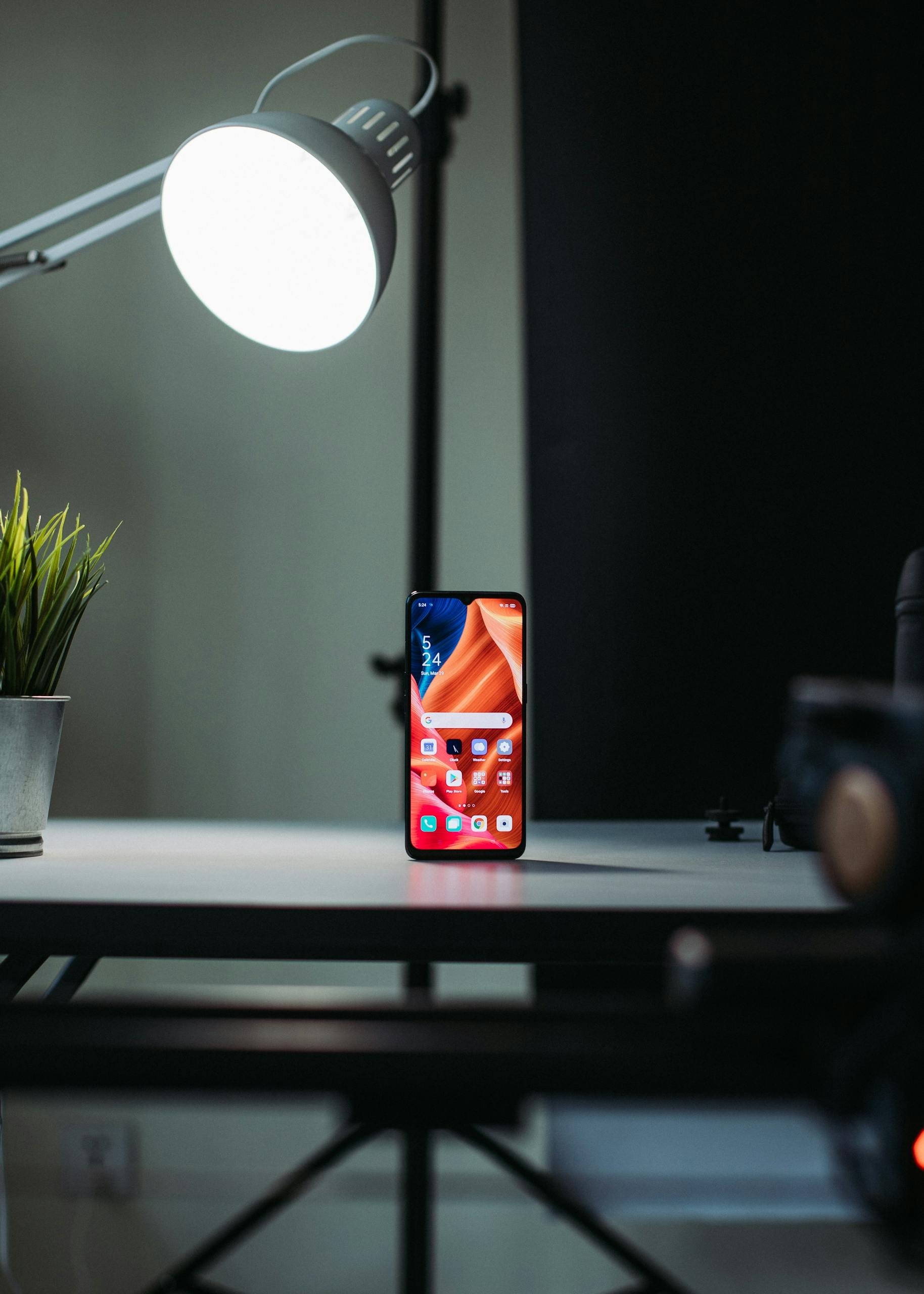 A modern smartphone placed vertically on a desk illuminated by a desk lamp, highlighting technology and lifestyle.